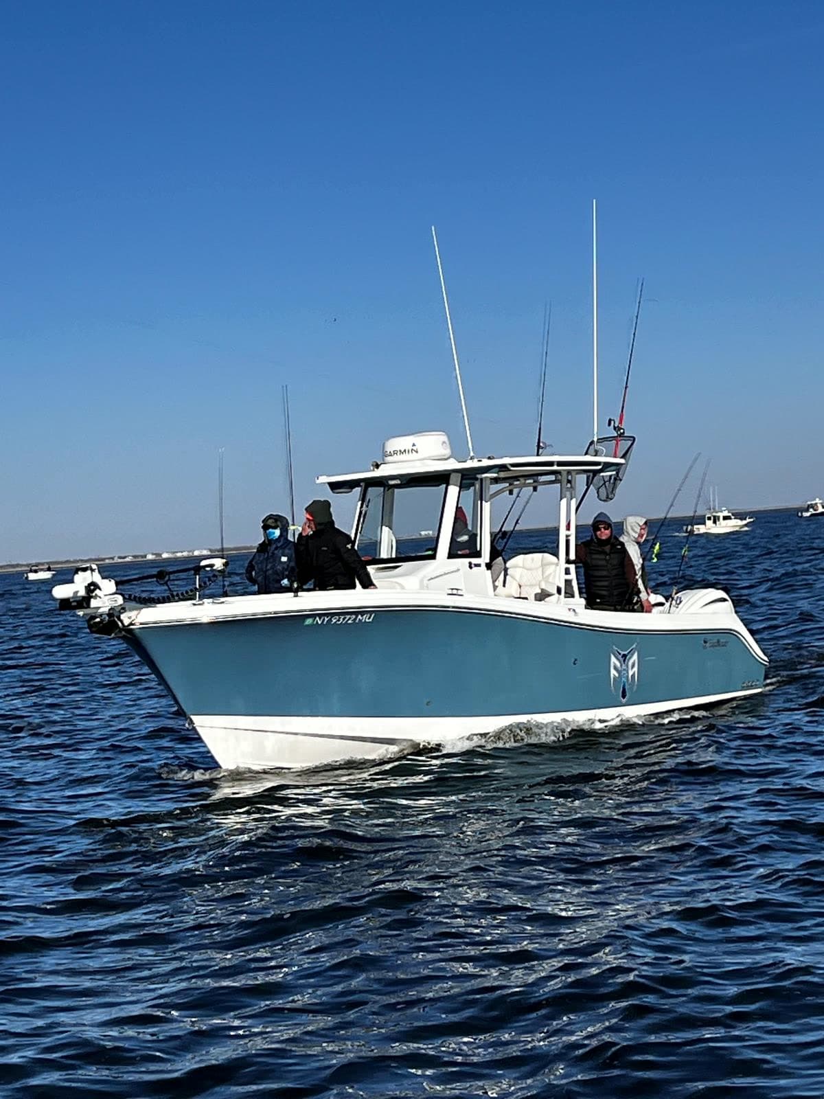 The Fishing The Atlantic boat underway on flat water — teal hull, white topsides, hardtop with radar, rods in the holders and anglers aboard.