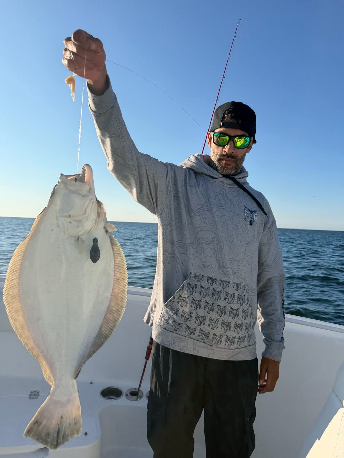 An angler holding a fluke up by the leader against a flat calm sea.